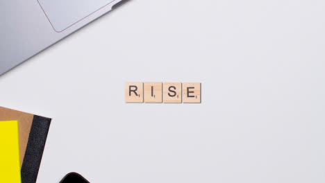 Stop-Motion-Business-Concept-Above-Desk-Wooden-Letter-Tiles-Forming-Word-Rise