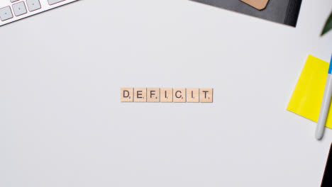 Stop-Motion-Business-Concept-Above-Desk-Wooden-Letter-Tiles-Forming-Word-Deficit