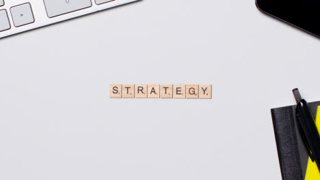 Stop-Motion-Business-Concept-Above-Desk-Wooden-Letter-Tiles-Forming-Word-Strategy