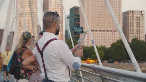 Man-Recording-Video-On-Mobile-Phone-Using-Gimbal-From-Hungerford-Bridge-Over-Thames-London-England-UK