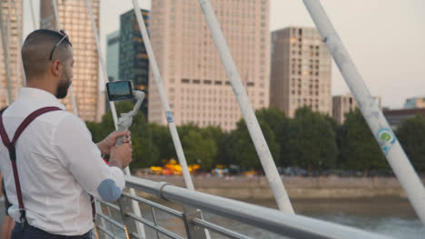 Man-Recording-Video-On-Mobile-Phone-Using-Gimbal-From-Hungerford-Bridge-Over-Thames-London-England-UK