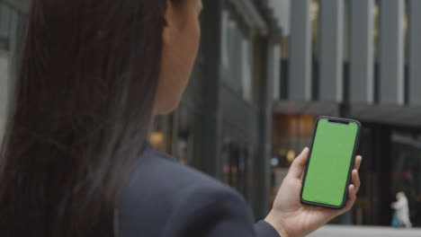 Businesswoman-Outside-City-Of-London-Offices-Holding-Green-Screen-Mobile-Phone-1