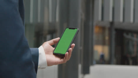 Businessman-Outside-City-Of-London-Offices-Holding-Green-Screen-Mobile-Phone
