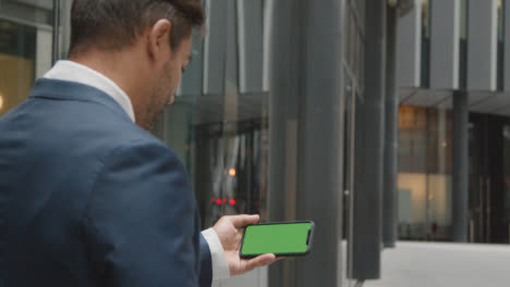 Businessman-Outside-City-Of-London-Offices-Holding-Green-Screen-Mobile-Phone-Horizontally