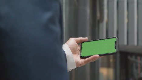 Businessman-Outside-City-Of-London-Offices-Holding-Green-Screen-Mobile-Phone-Horizontally-2