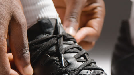 Studio-Close-Up-Of-Male-Footballer-Or-Sportsperson-Tying-Laces-On-Boots-Or-Training-Shoes