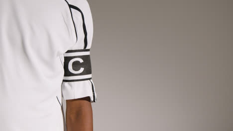 Close-Up-Studio-Shot-Of-Male-Footballer-Wearing-Club-Kit-And-Captains-Armband