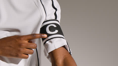 Close-Up-Studio-Shot-Of-Male-Footballer-Wearing-Club-Kit-Pointing-At-Captains-Armband