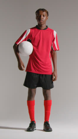 Vertical-Video-Studio-Portrait-Of-Young-Male-Footballer-Wearing-Club-Kit-With-Ball-Under-Arm-1