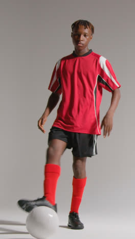 Vertical-Video-Studio-Portrait-Of-Young-Male-Footballer-Wearing-Club-Kit-With-Ball-Under-Arm-2