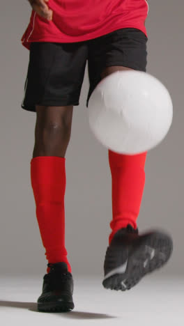 Vertical-Video-Close-Up-Studio-Shot-Of-Male-Footballer-In-Studio-Playing-Keepy-Uppy-Kicking-Ball-