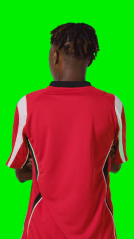 Vertical-Video-Rear-View-Of-Young-Male-Footballer-Wearing-Club-Kit-Watching-Game-Against-Green-Screen