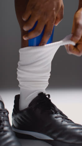 Vertical-Video-Studio-Close-Up-Of-Male-Footballer-Or-Sportsperson-Putting-Shin-Guards-Into-Socks-1