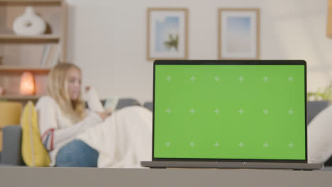 Woman-Relaxing-On-Sofa-Using-Mobile-Phone-At-Home-With-Green-Screen-Laptop-In-Foreground-