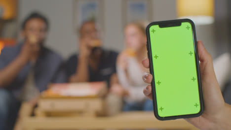 Friends-At-Home-Sitting-On-Sofa-Eating-Pizza-With-Green-Screen-Mobile-Phone-In-Foreground-1