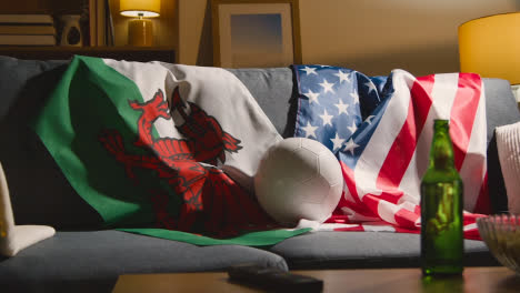 Sofa-In-Der-Lounge-Mit-Amerikanischen-Und-Walisischen-Flaggen-Und-Ball,-Während-Sich-Die-Fans-Darauf-Vorbereiten,-Fußballspiele-Im-Fernsehen-Zu-Sehen