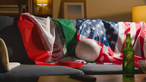Sofa-In-Der-Lounge-Mit-Amerikanischen-Und-Iranischen-Flaggen-Und-Ball,-Während-Sich-Die-Fans-Darauf-Vorbereiten,-Fußballspiele-Im-Fernsehen-Zu-Sehen