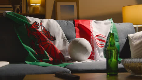 Sofa-In-Der-Lounge-Mit-Walisischen-Und-Iranischen-Flaggen-Und-Ball,-Während-Sich-Die-Fans-Darauf-Vorbereiten,-Fußballspiele-Im-Fernsehen-Zu-Sehen