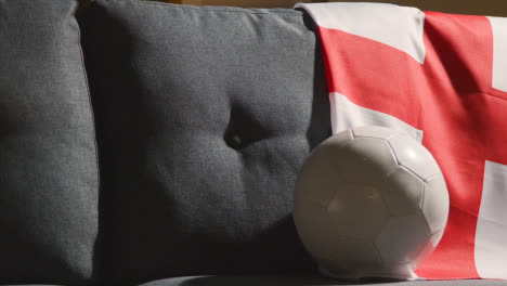 Sofa-In-Der-Lounge-Mit-Englischer-Flagge-Und-Ball,-Während-Sich-Die-Fans-Darauf-Vorbereiten,-Ein-Fußballspiel-Auf-Tv-1-Zu-Sehen
