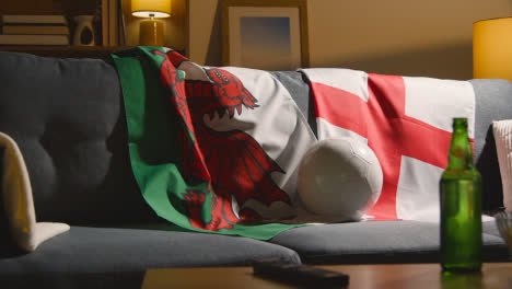 Sofa-In-Lounge-With-English-And-Welsh-Flags-And-Ball-As-Fans-Watch-Football-Soccer-Match-On-TV