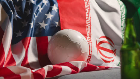 Sofa-In-Der-Lounge-Mit-Iranischen-Und-Amerikanischen-Flaggen-Und-Ball,-Während-Fans-Fußballspiele-Im-Fernsehen-Sehen-3