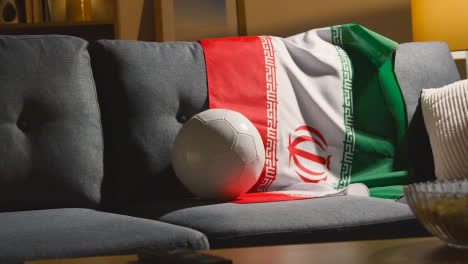 Sofa-In-Der-Lounge-Mit-Iranischer-Flagge-Und-Ball,-Während-Sich-Die-Fans-Darauf-Vorbereiten,-Fußballspiele-Im-Fernsehen-Zu-Sehen-2