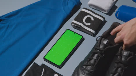 Studio-Flat-Lay-Shot-Of-Football-Soccer-Boots-Shirt-Captains-Armband-Shin-Guards-And-Mobile-Phone-