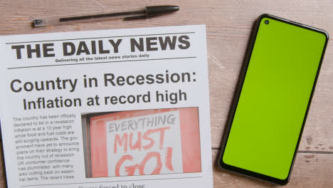 Zeitung-Mit-Schlagzeile-über-Rezession-Neben-Greenscreen-Handy-Mit-Handscrolling