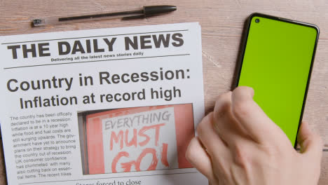 Zeitung-Mit-Schlagzeile-über-Rezession-Und-Inflation-Neben-Der-Hand,-Die-Ein-Green-screen-handy-Abholt