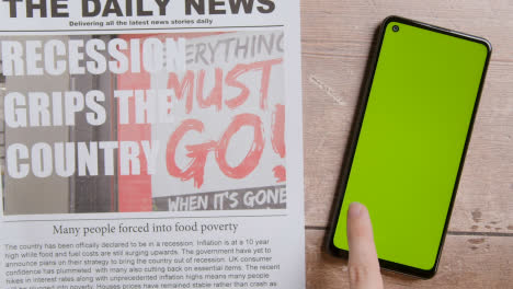 Newspaper-With-Headline-On-Recession-And-Inflation-Next-To-Hand-Putting-Down-Green-Screen-Mobile-Phone-