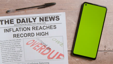 Newspaper-With-Headline-On-Recession-Next-To-Green-Screen-Mobile-Phone-With-Hand-Scrolling-1