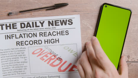 Newspaper-With-Headline-On-Inflation-Next-To-Hand-Picking-Up-Green-Screen-Mobile-Phone-