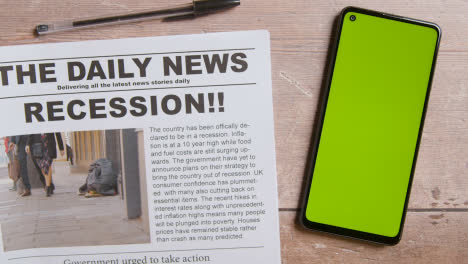Newspaper-With-Headline-On-Recession-Next-To-Green-Screen-Mobile-Phone-With-Hand-Scrolling-1