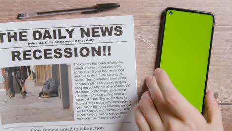 Zeitung-Mit-Schlagzeile-über-Rezession-Neben-Hand,-Die-Handy-Mit-Grünem-Bildschirm-In-Die-Hand-Nimmt-1