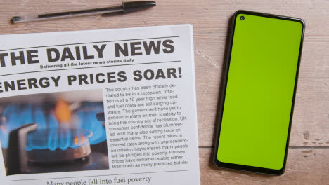 Newspaper-With-Headline-On-Energy-Price-Crisis-Next-To-Green-Screen-Mobile-Phone-With-Hand-Scrolling-1