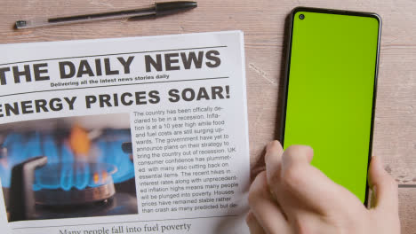 Newspaper-With-Headline-On-Energy-Price-Crisis-Next-To-Hand-Picking-Up-Green-Screen-Mobile-Phone-