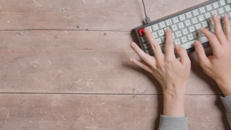 Overhead-Shot-Of-Hands-Typing-On-Computer-Keyboard-On-Wooden-Desk-At-Home