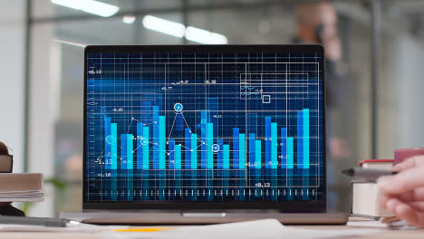 Laptop-Auf-Dem-Schreibtisch-In-Einem-Geschäftigen-Modernen-Büro-Mit-Animierten-Finanzdiagrammen-Und-Diagrammen