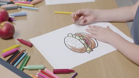 Primer-Plano-De-Un-Niño-En-Casa-Coloreando-La-Imagen-De-Una-Hamburguesa-En-La-Mesa-1