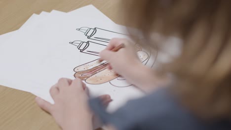 Close-Up-Of-Child-At-Home-Colouring-In-Picture-Of-Hot-Dog-At-Table-