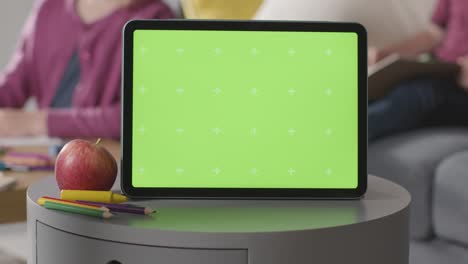 Nahaufnahme-Eines-Digitalen-Green-Screen-Tablets-Mit-Kindern,-Die-Im-Hintergrund-Färben-Und-Lesen
