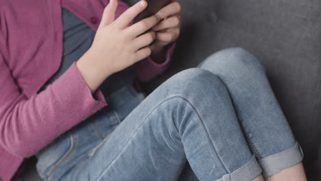 Primer-Plano-De-Una-Chica-Sentada-En-Un-Sofá-En-Casa-Mirando-En-Línea-Usando-El-Teléfono-Móvil-1