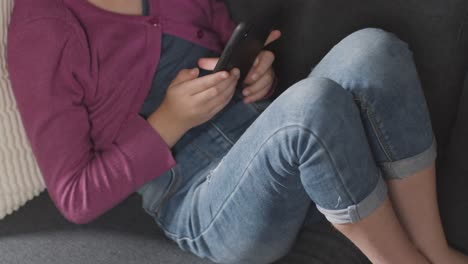 Close-Up-Of-Girl-Sitting-On-Sofa-At-Home-Looking-Online-Using-Mobile-Phone-3