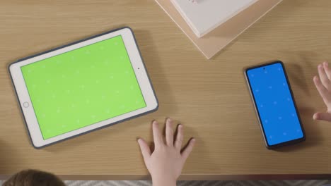 Overhead-Shot-Of-Children-Using-Green-Screen-Digital-Tablet-And-Blue-Screen-Mobile-Phone-On-Table-At-Home-1