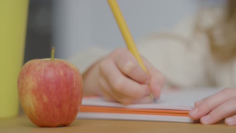 Nahaufnahme-Von-Kind-In-Buch-Am-Tisch-Mit-Apfel-Im-Vordergrund-Schreiben
