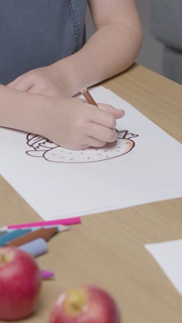 Vertical-Video-Close-Up-Of-Child-At-Home-Colouring-In-Picture-Of-Burger-At-Table-With-Apple-In-Foreground