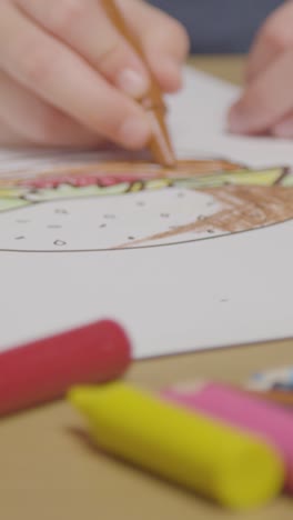 Vertical-Video-Close-Up-Of-Child-At-Home-Colouring-In-Picture-Of-Burger-At-Table