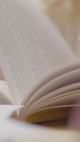 Vertical-video-Close-Up-Of-Child-Sitting-At-Table-At-Home-Reading-Book