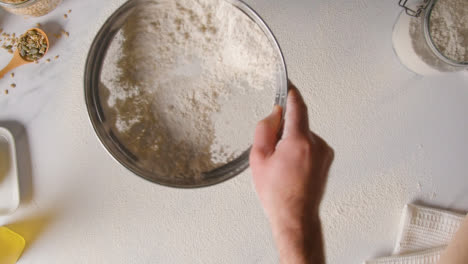 Overhead-Shot-Of-Freshly-Baked-Loaf-Of-Bread-Being-Put-Down-Onto-Marble-Surface-Covered-In-Flour