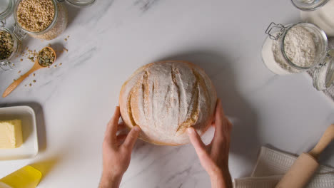 Overhead-Shot-Of-Freshly-Baked-Loaf-Of-Bread-Being-Put-Down-Onto-Marble-Work-Surface-1